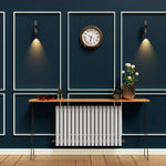 Modern interior design with a clock, radiator, and decorative items against a dark blue wall.

